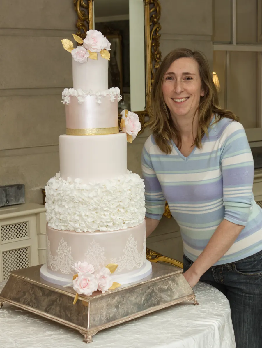Susie Coffey beside a five-tier blush and gold wedding cake